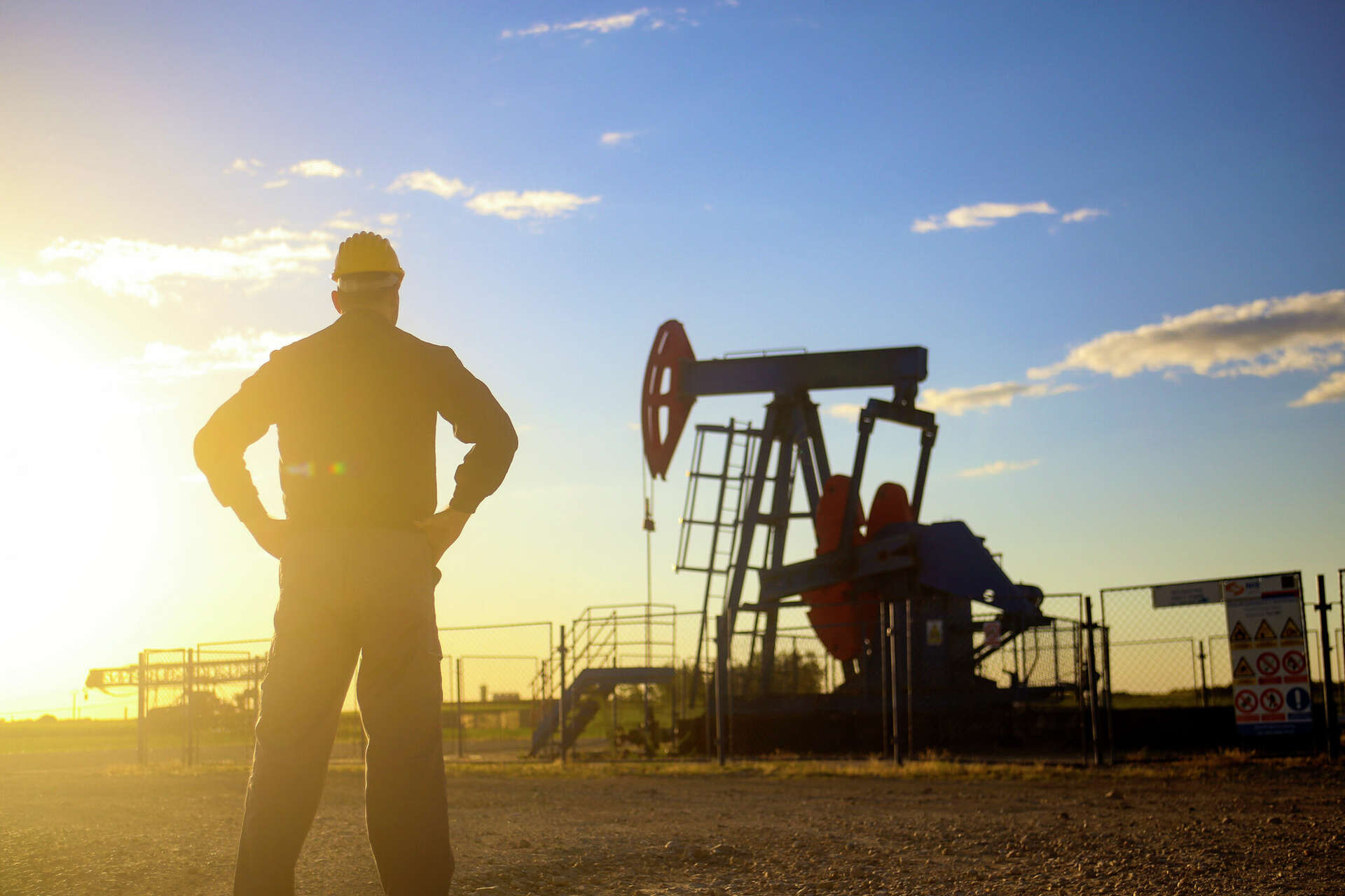 Oil worker facing a pumpjack at sunset in the Permian Basin