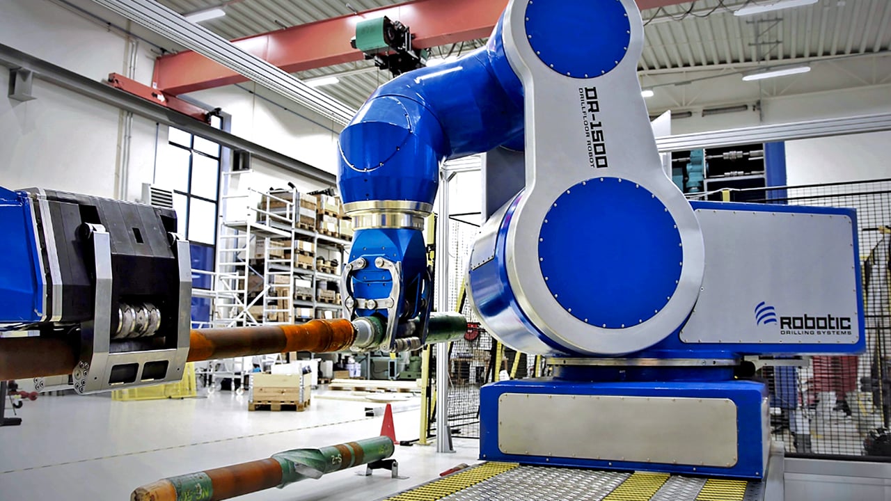 A large industrial robotic arm labeled DR-1500 is operating in a factory setting, gripping a pipe.
